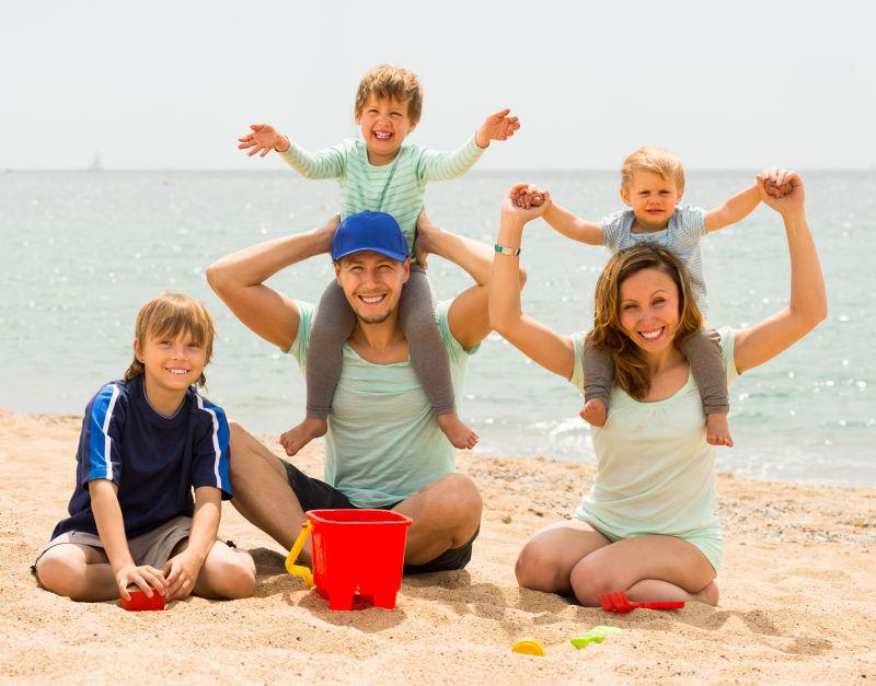 在海边度假的父母微笑着带着三个孩子
