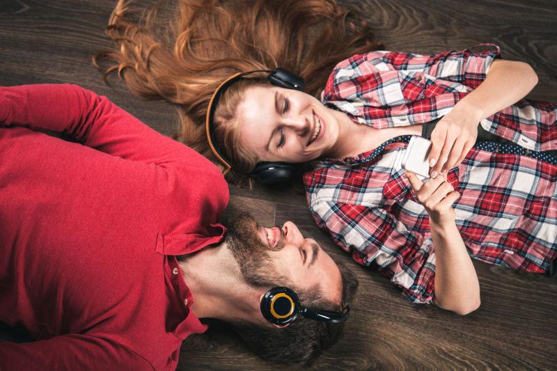 戴着耳机躺在木板上听音乐的年轻夫妇