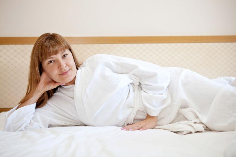 年轻女人穿着一件白色长袍躺在床上