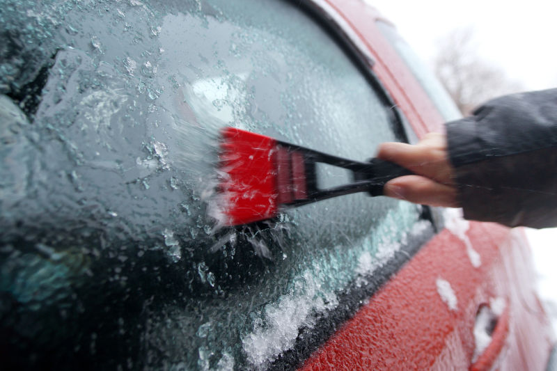 用工具铲除冰雪覆盖的车窗
