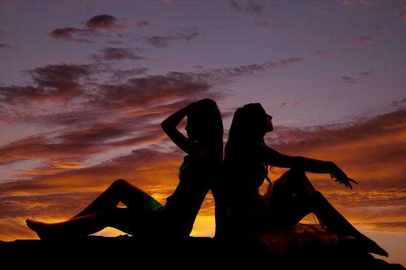 晚霞中背靠背坐在一起的两个女人