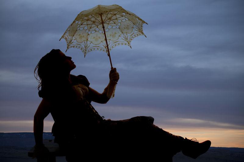 黄昏背景中带着伞的女人