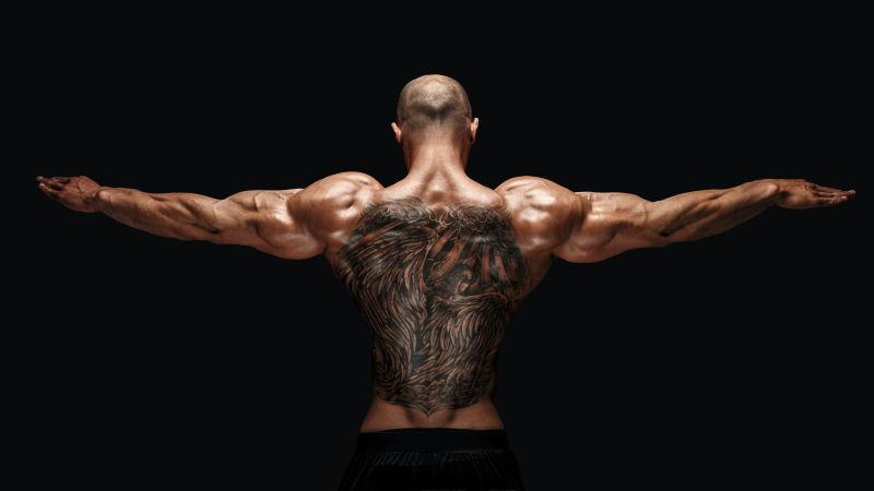 纹身健美运动员在黑色背景上伸出手臂