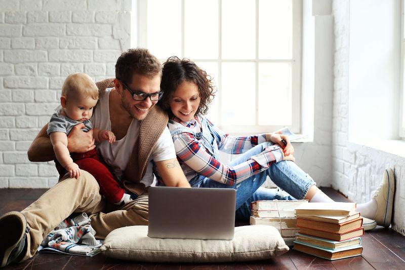 在地板上看笔记本电脑的年轻快乐的家庭