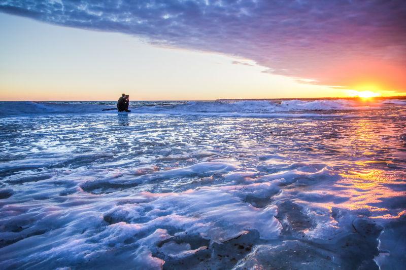 一位年轻的摄影师在冰冻的湖面上拍摄日落