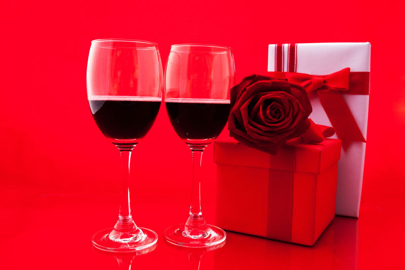 红色背景上的红酒玫瑰礼物盒还有贺卡
