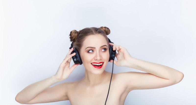 白色背景下使用耳机听音乐的年轻性感美女