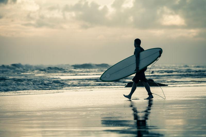 夕阳下的海滩上男人拿着一块冲浪板
