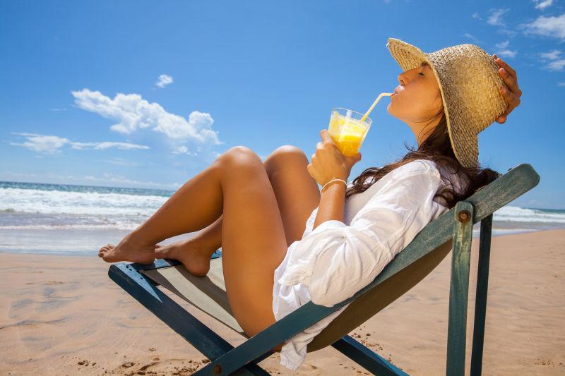 沙滩上戴着草帽的年轻女子在喝菠萝汁