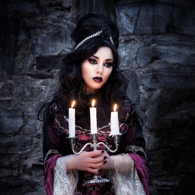 黑色背景中拿着燃烧蜡烛的哥特女孩