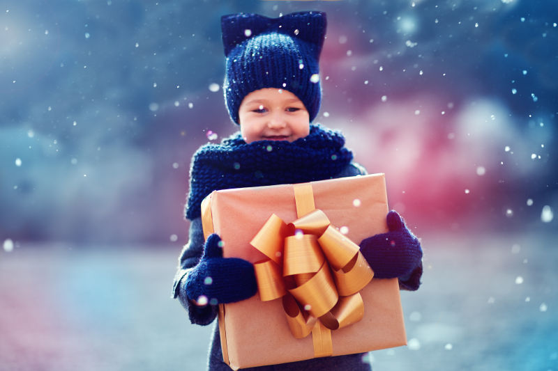 一个可爱的孩子在下雪天抱着超大的礼盒