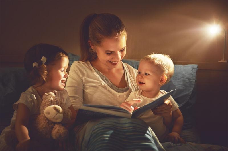 快乐的家庭母亲和孩子们在床上看书