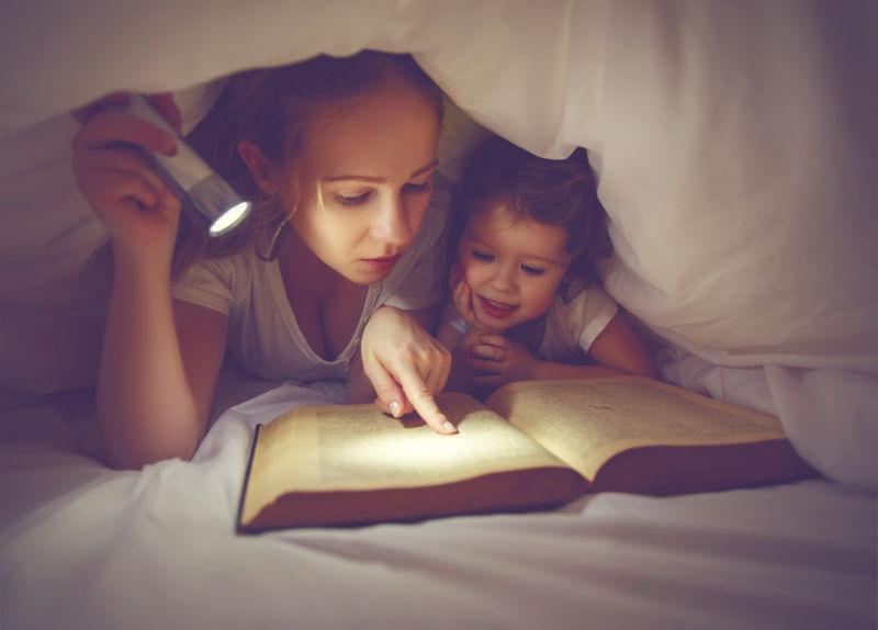 妈妈和女儿在床上用手电筒看书