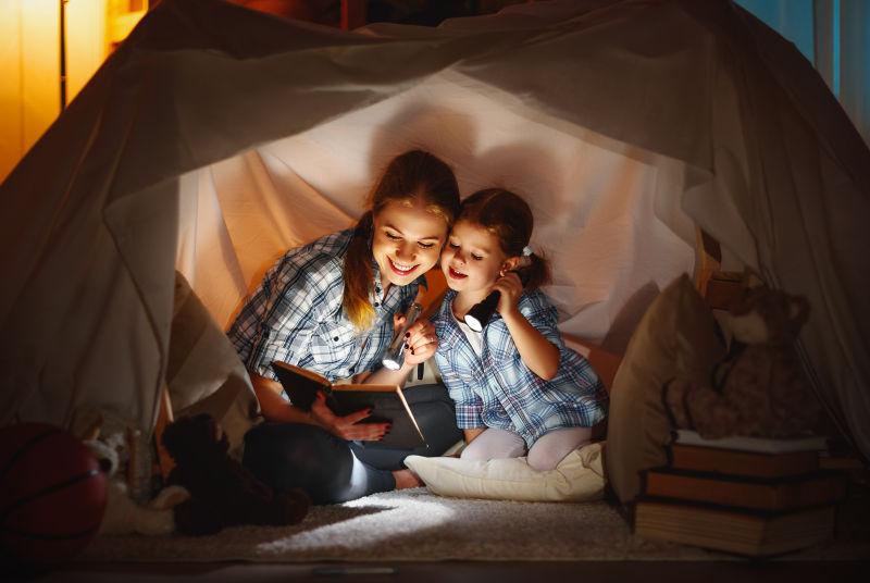 帐篷里用手电筒看书的母女