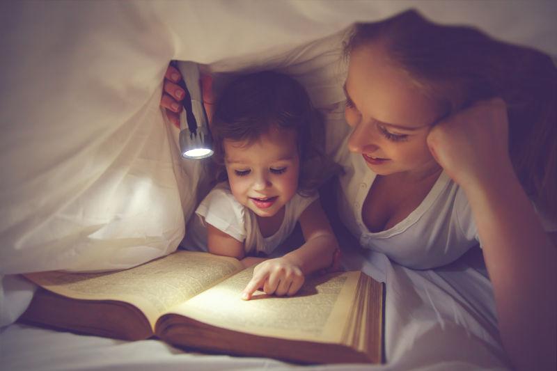 妈妈和孩子在床上用手电筒读书