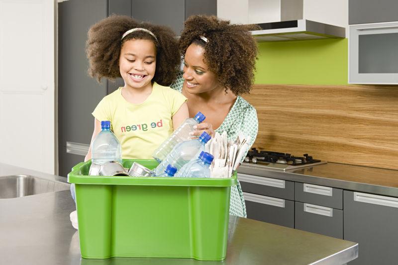 黑人妇女和她女儿在厨房整理绿色箱子里的可回收垃圾