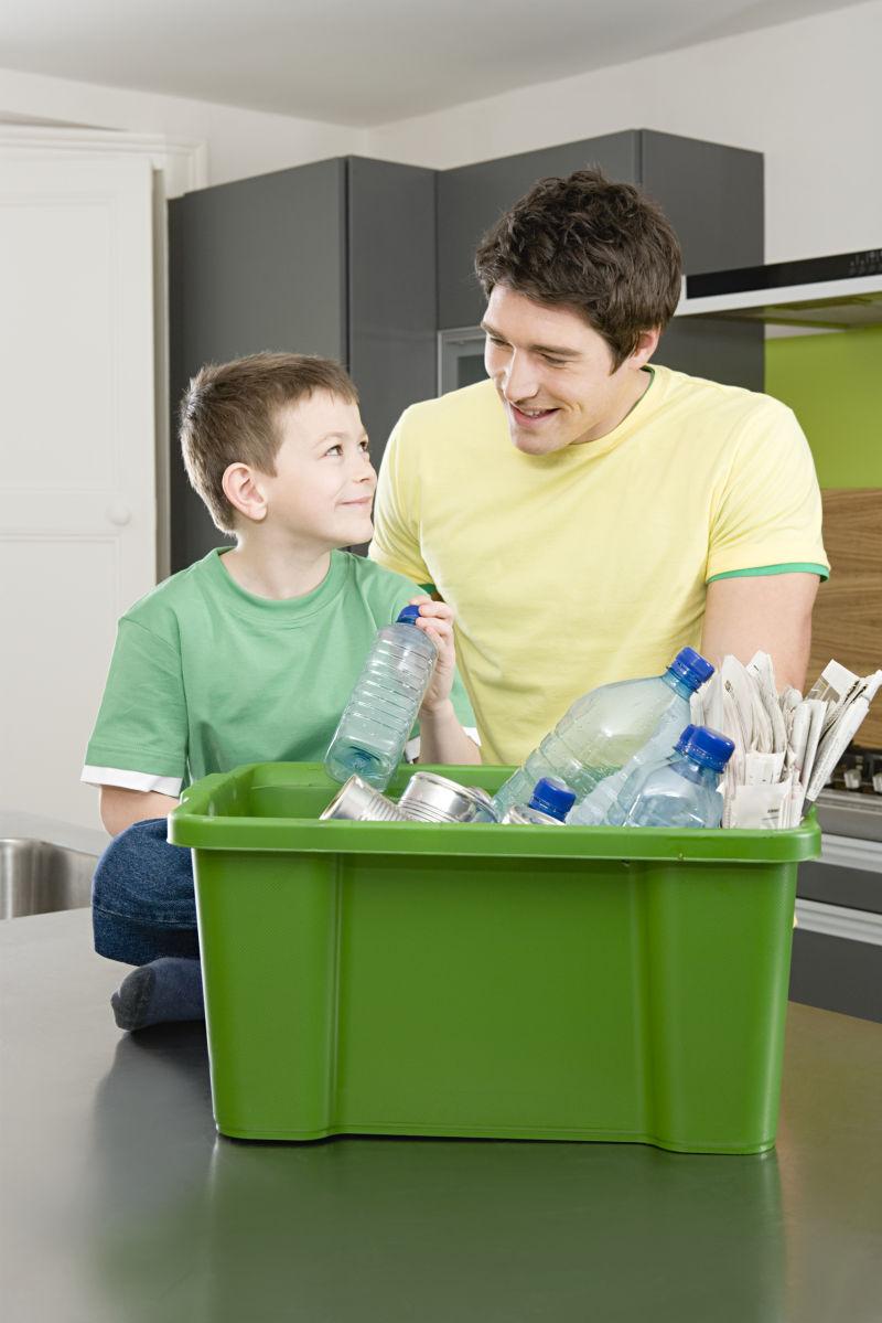 白人父子在整理桌子上装着可回收垃圾的绿色箱子