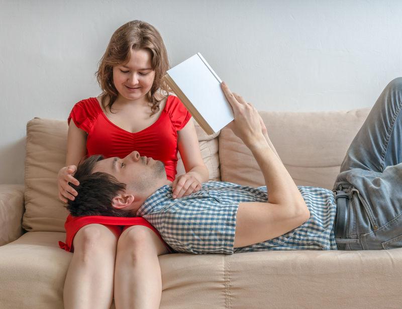 在客厅的沙发上躺在妻子腿上看书的丈夫