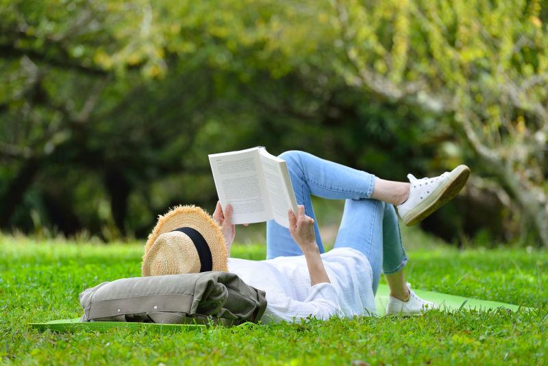 躺在绿色的草地上看书的年轻人