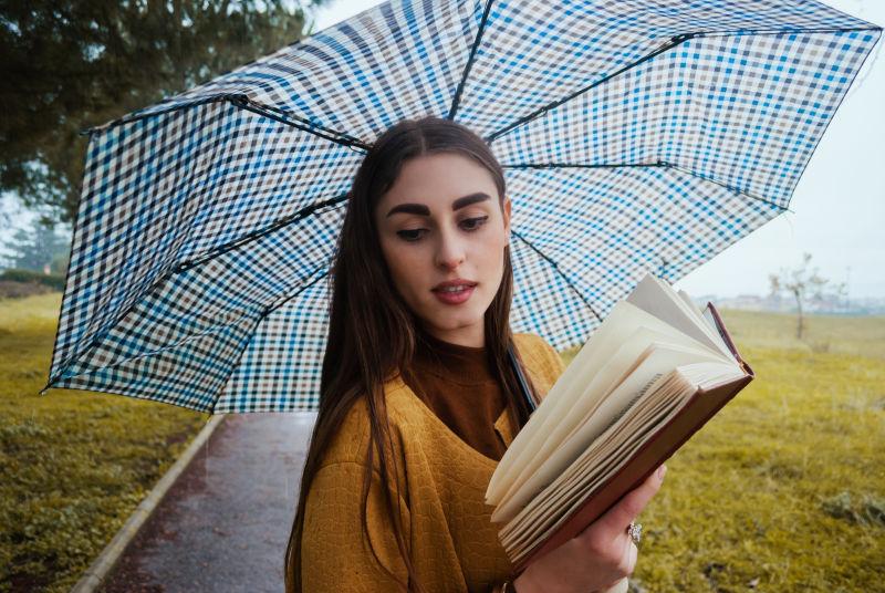 在户外打着伞看书的年轻女孩