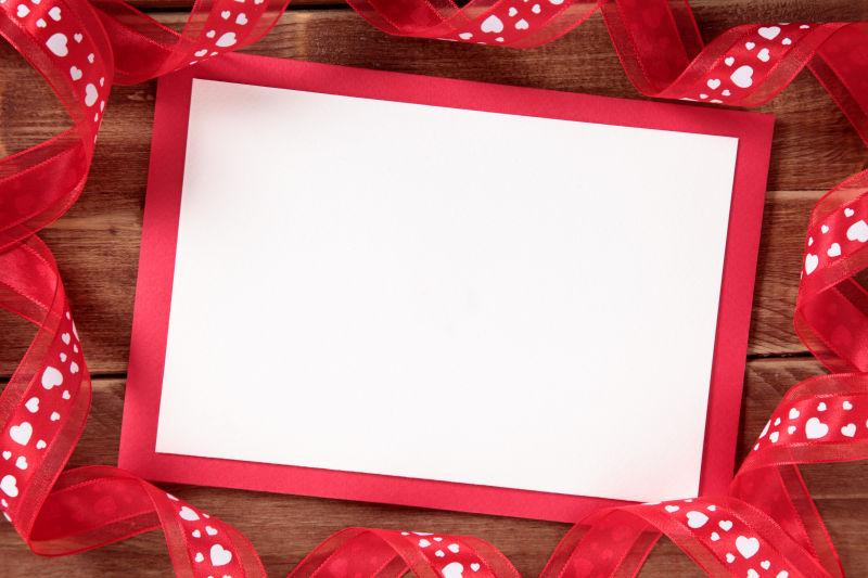 木板上的浪漫情人节卡片和红色丝带