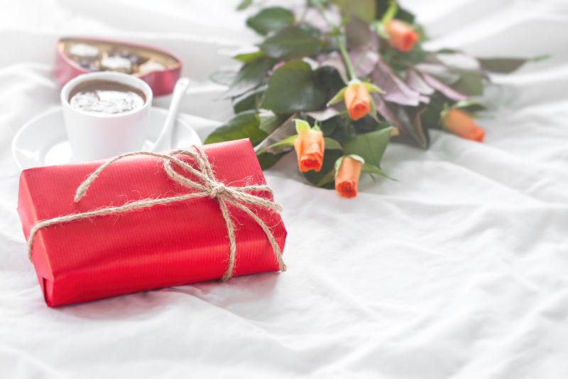 白色床单上的花束和咖啡还有巧克力和红色礼物盒