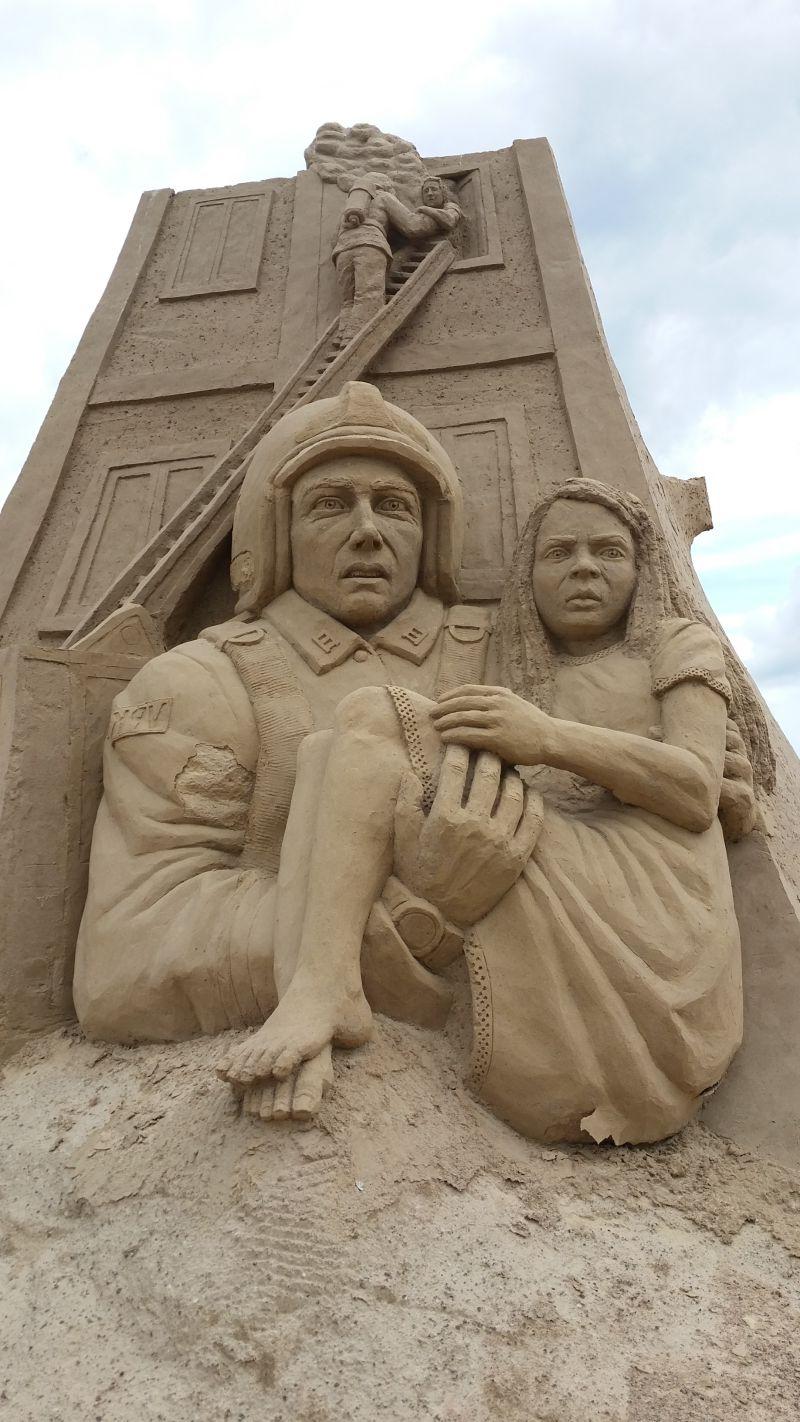 沙滩上的抱着女人的救火员沙子雕塑