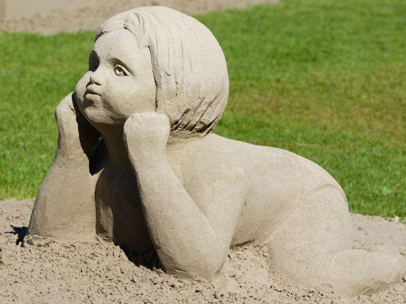 沙滩上的趴着撑着下巴的可爱男孩雕塑
