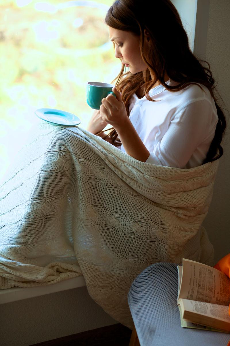 窗户边的美女喝着咖啡看着书