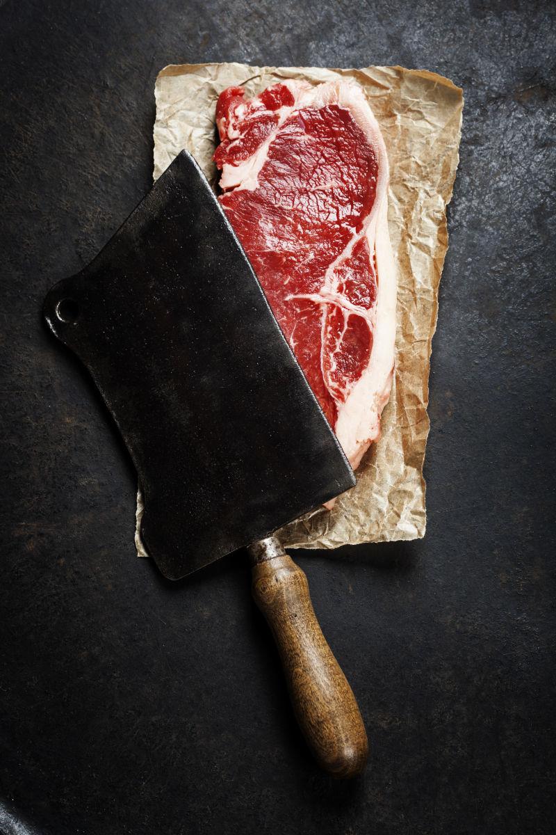 老式的切肉刀和生牛排在黑暗的背景中