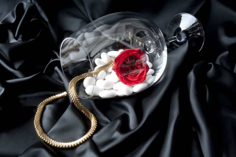 黑色绸缎上的透明杯子里的玫瑰花和金色项链
