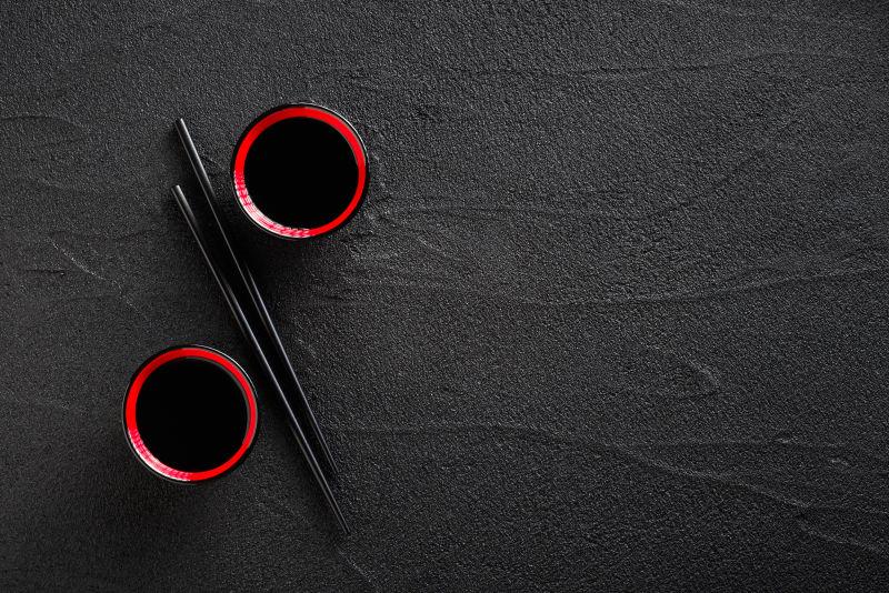 黑色桌面上的两个酱油碗和筷子
