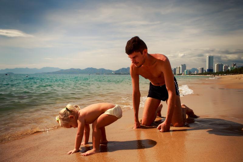 欧洲年轻父亲蹲在沙滩上带小女儿玩耍
