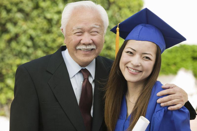 快乐的女毕业生和爷爷站在户外的画像