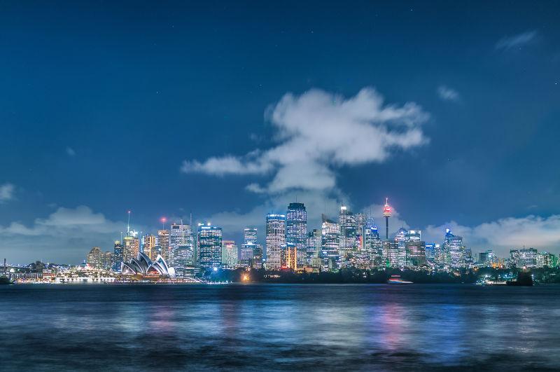 蓝天白云下的亮着灯的歌剧院和城市悉尼塔