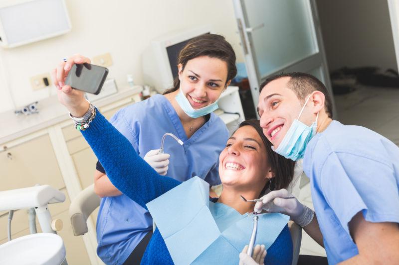快乐的病人和牙医拿着智能手机自拍