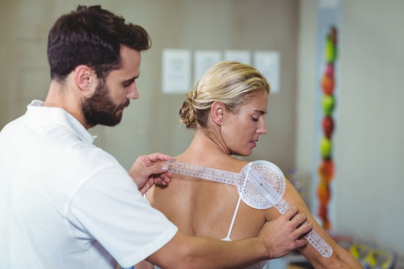 男性治疗师用测角仪测量女性患者肩部