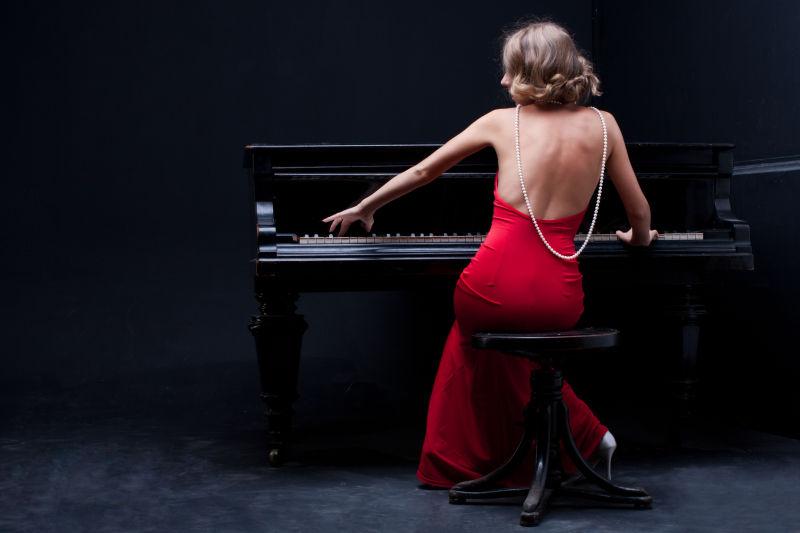 穿着红色露背礼服的金发美女弹钢琴