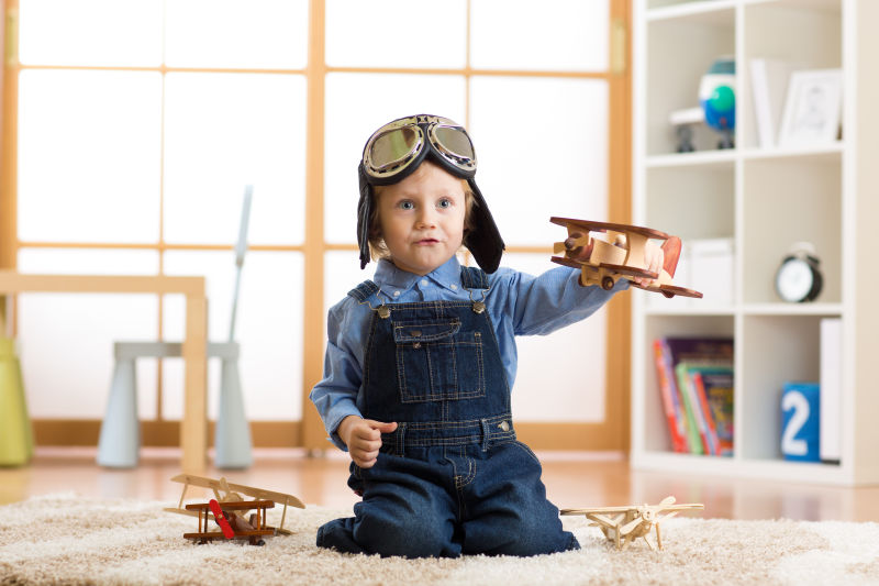 跪在地毯上玩着木质飞机的小男孩