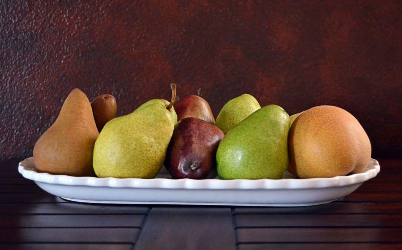 木桌上白色盘子里的不同品种的五颜六色的梨子