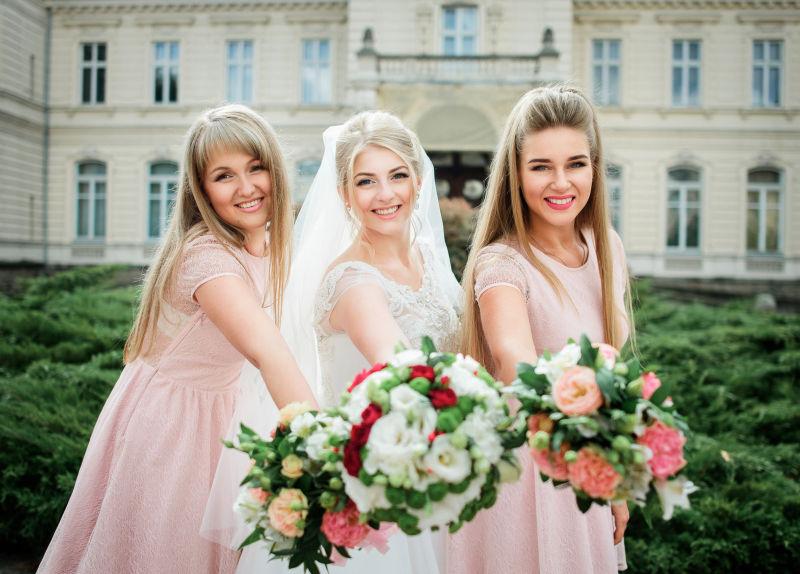 伴娘穿着粉色衣服和新娘双手捧着结婚花束