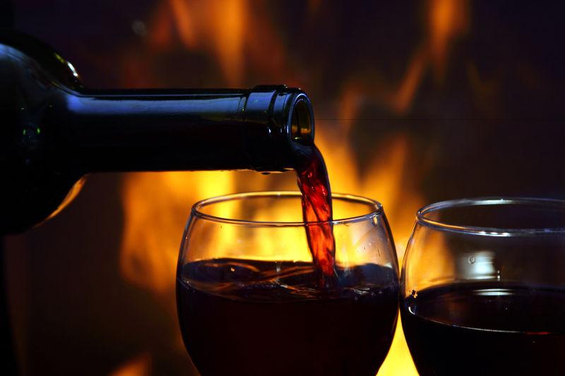 燃烧着的壁炉前向高脚杯里注入红葡萄酒