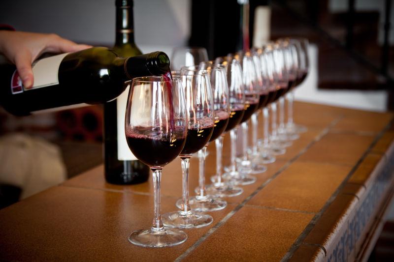 木桌上向排列整齐的高脚杯中注入红葡萄酒
