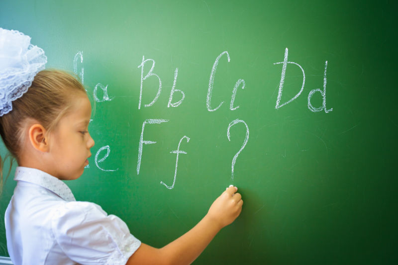 女学生在黑板上用粉笔写英语字母表