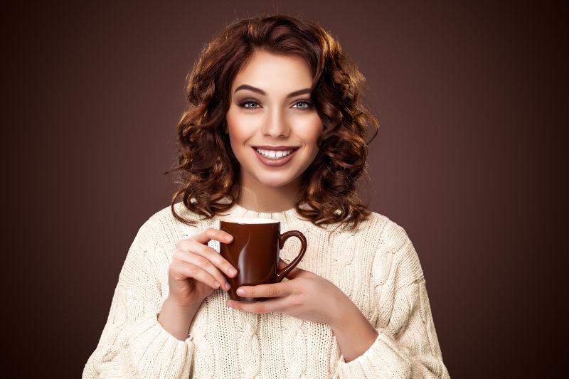 棕色背景上拿着咖啡杯的美女