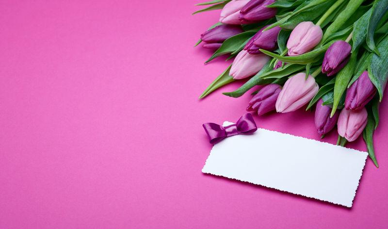 粉红色背景中绸缎蝴蝶结装饰的卡片和鲜花
