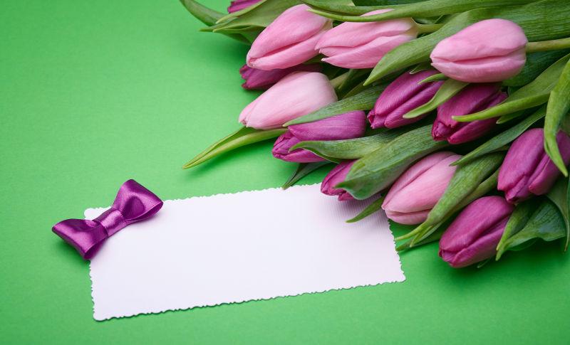 绿色背景中的紫色郁金香和带有蝴蝶结的卡片