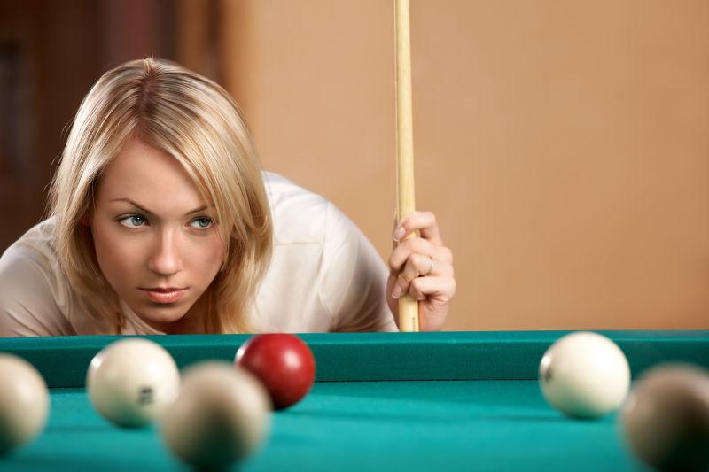 褐色背景下拿着球杆望向球桌计算弹道的美女