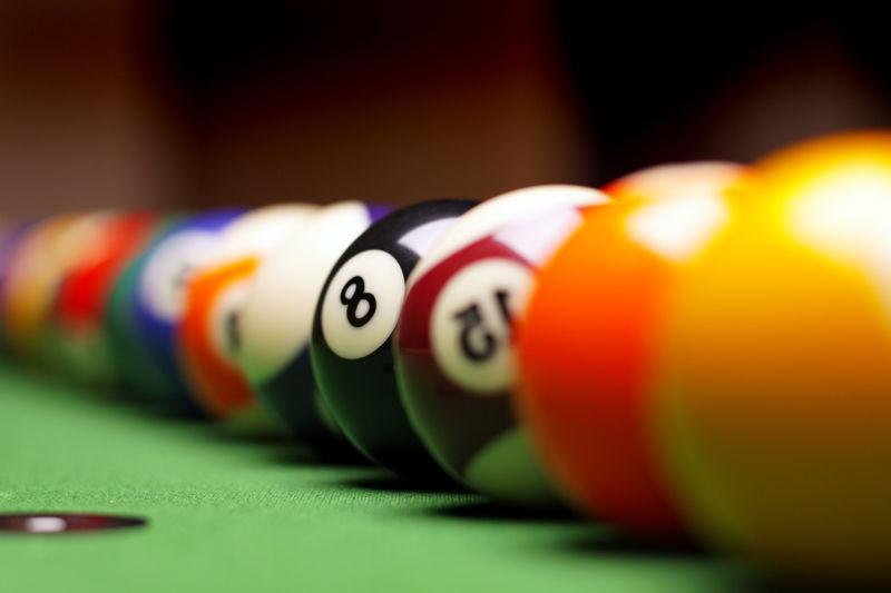 褐色背景下绿色球桌上整齐排成一行的台球
