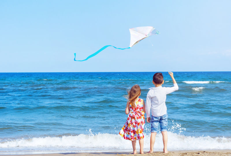 在海边拿着风筝的男孩和女孩